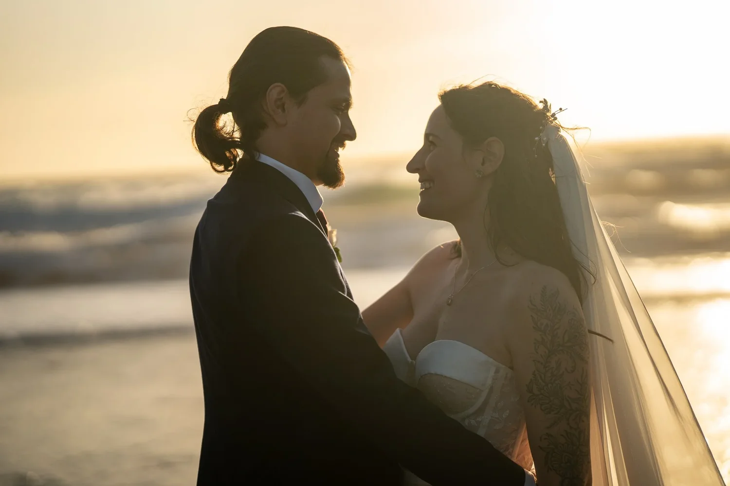 Newlyweds facing each other at sunset with the sea behind them
