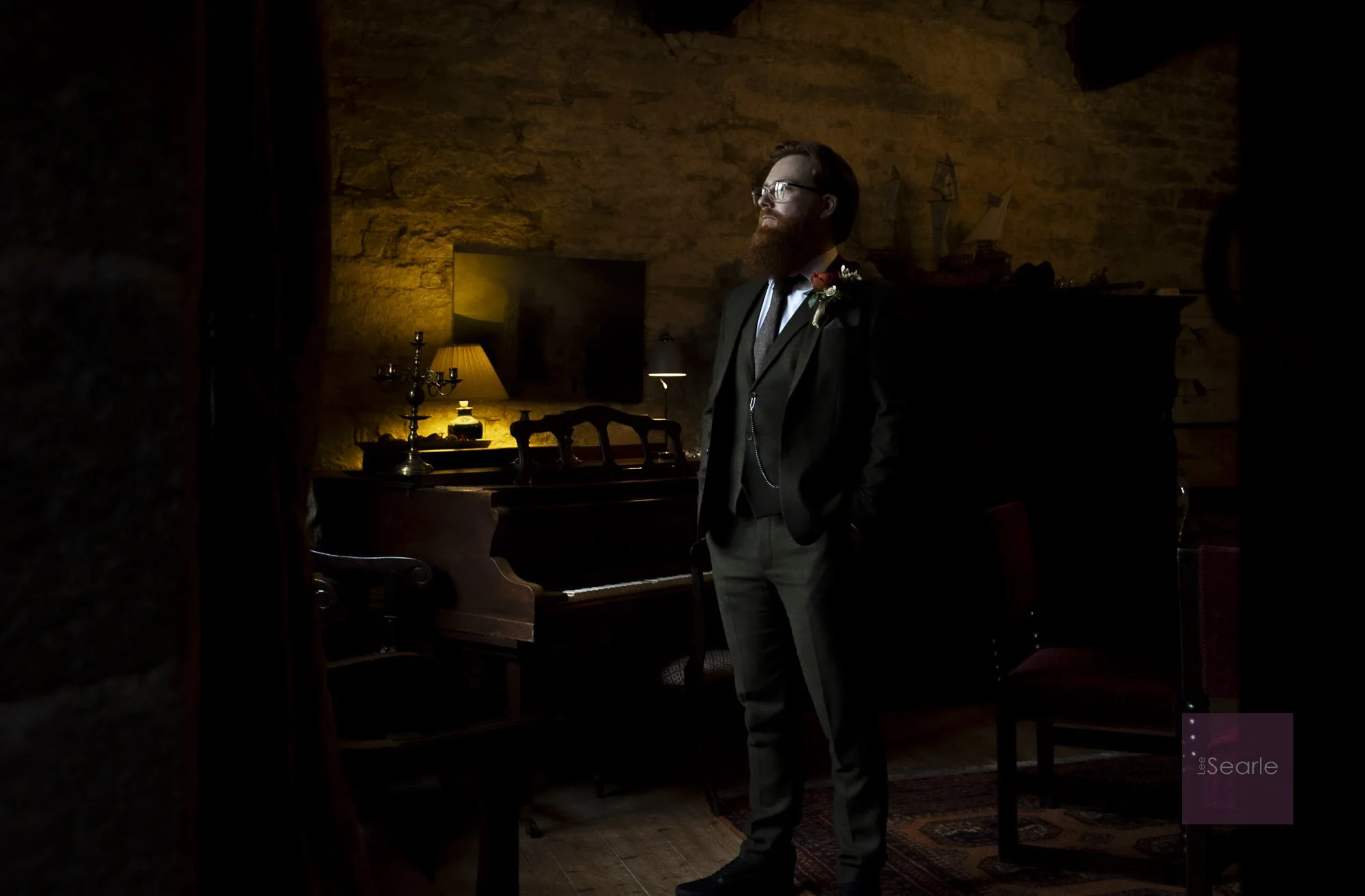 Groom waiting by the piano in the candlelit hall at Pengersick Castle