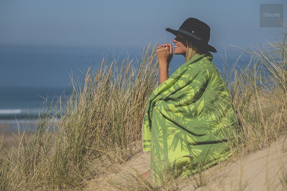 Woman wrapped in a green Atlantic Blankets throw in the dunes, Cornwall lifestyle product photography