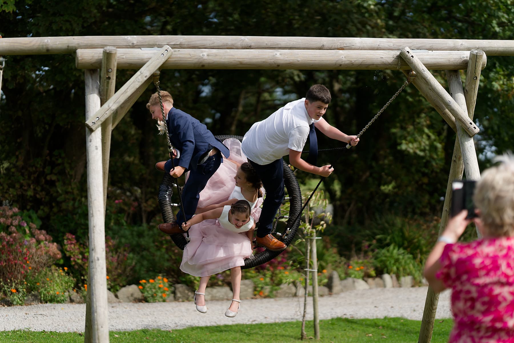 Children from the wedding party piling onto a garden swing at a Cornwall wedding