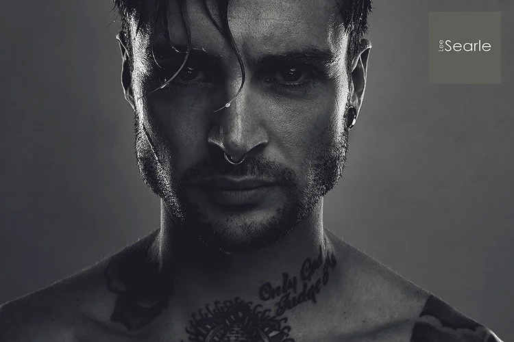Moody black and white portrait with hard light and shadow across a tattooed man