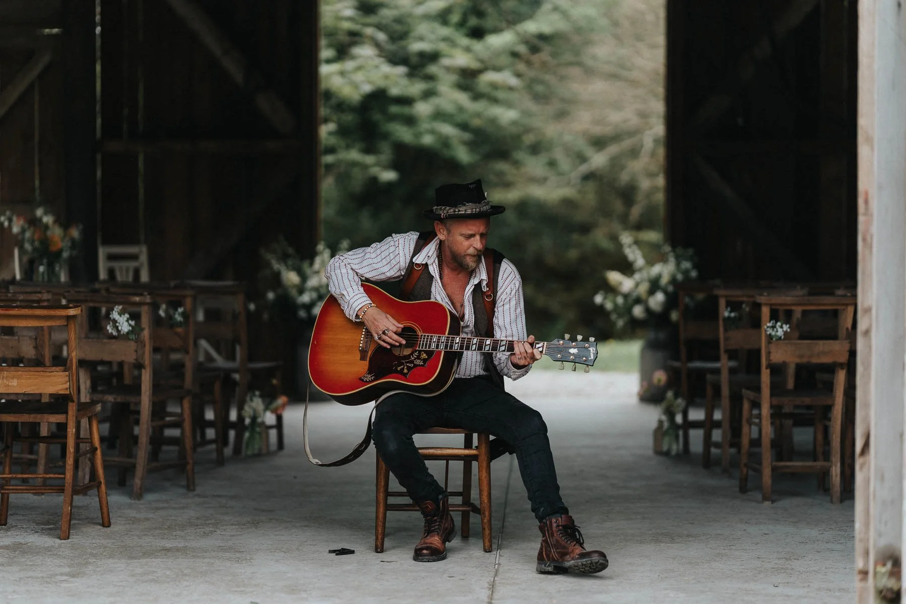 Lee Searle, wedding photographer based in Penzance, Cornwall, sitting in a barn with his red acoustic guitar