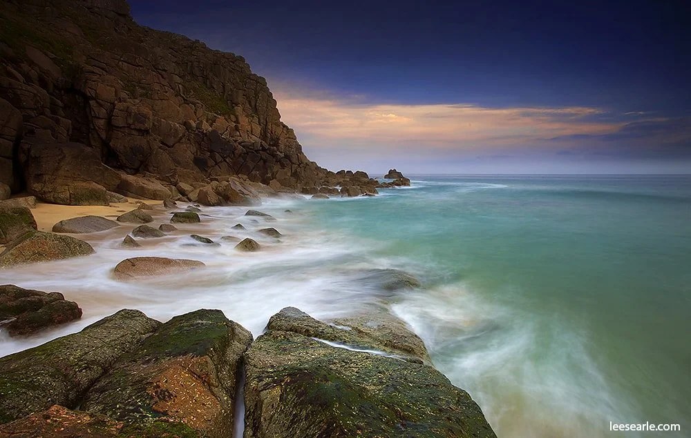 Turquoise sea washing over granite rocks beneath the cliffs near Porthcurno, Cornwall