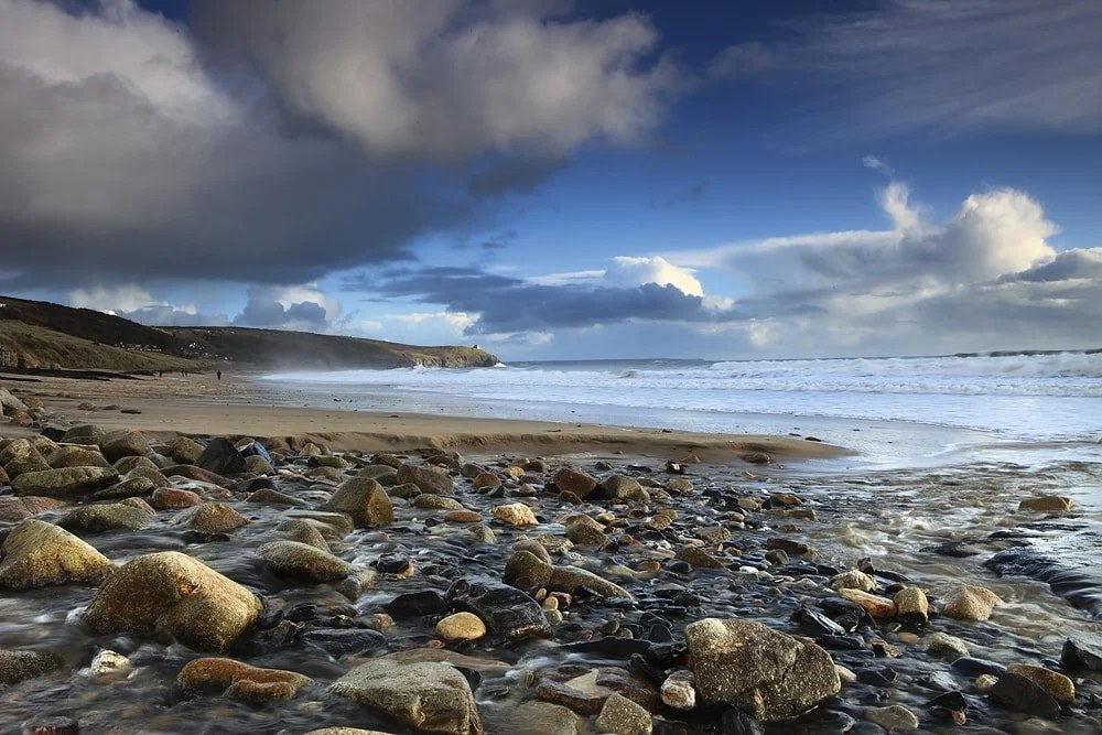 Cornwall landscape photography: storm light breaking over a boulder-strewn beach on the west Cornwall coast