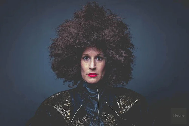 Bold studio portrait with wild hair and red lipstick against a dark blue backdrop