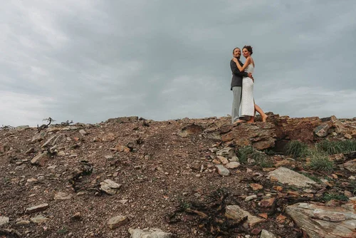 Two grooms embracing on the clifftop rocks under a grey sky