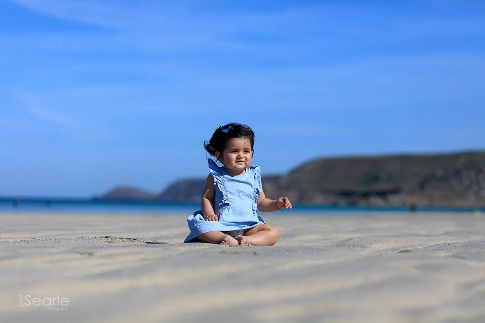 Baby sitting on the sand at the water's edge on a Cornish beach under a bright blue sky