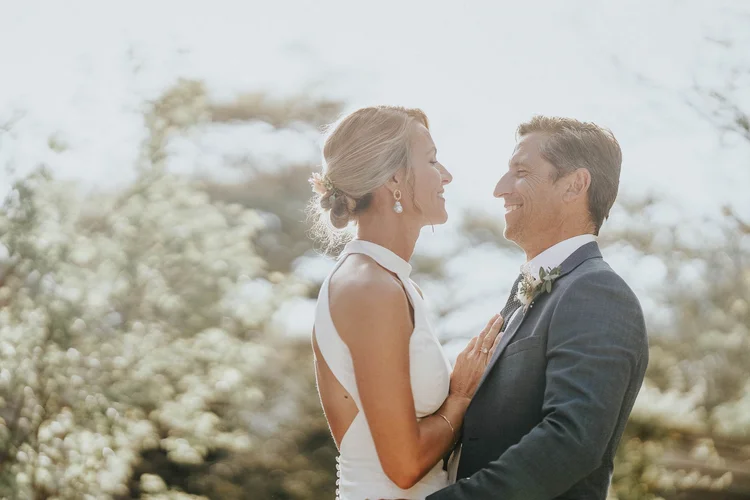 Bride and groom laughing together in the blossom, foreheads almost touching