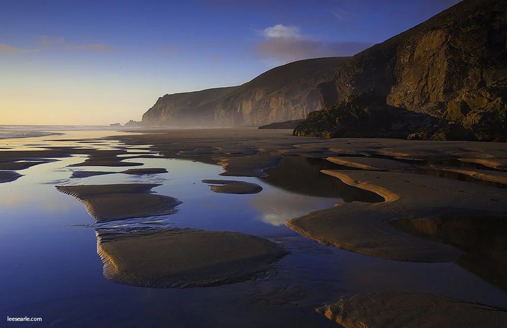 Rock pools reflecting first light beneath a headland on the north Cornwall coast
