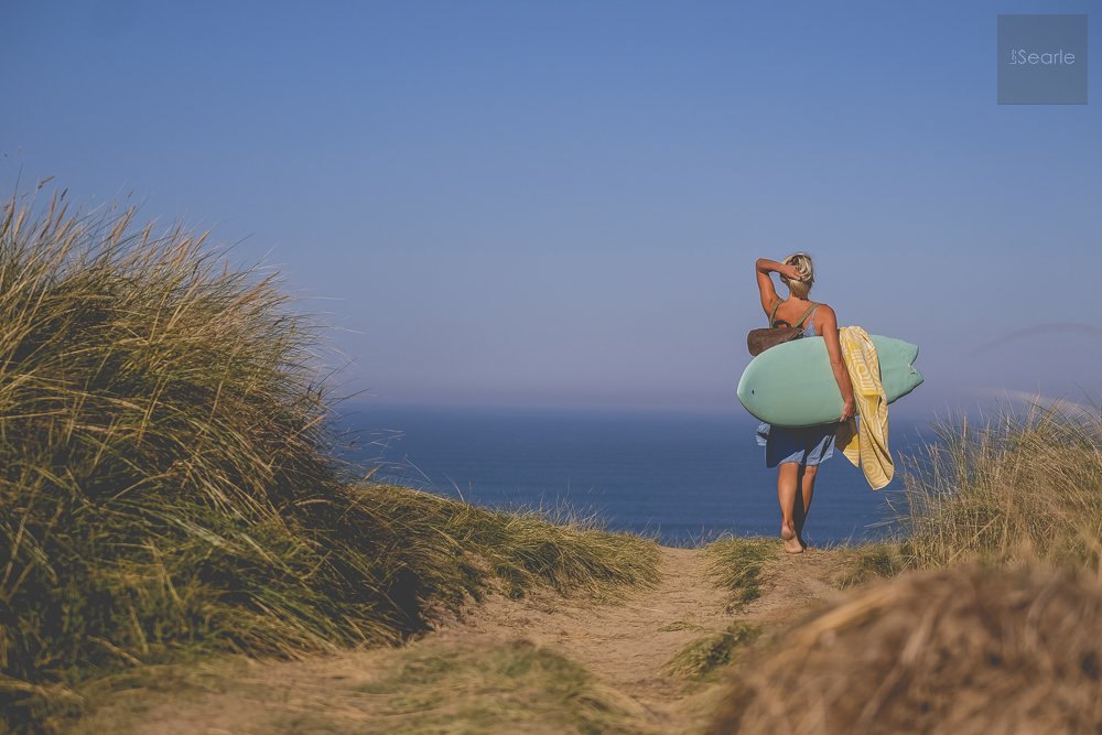 Surfer carrying a board and blanket over the dunes at sunset for a Cornish brand shoot